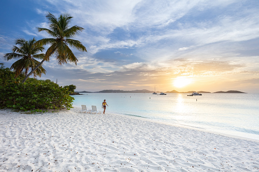 Walking bikini woman with lounge chairs and palm trees on a tropical beach Honeymoon Beach, St. John, United States Virgin Islands