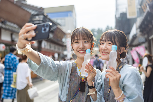 Young female friends in traditional Japanese Matsuri outfit taking selfie picture with soda pop on street