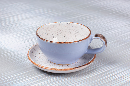 Empty ceramic cup and saucer on a gray background.