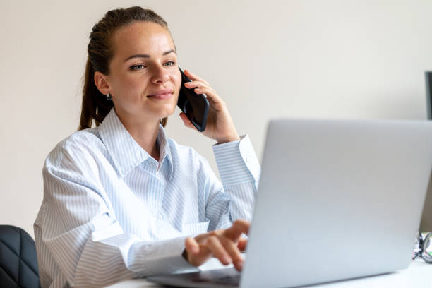 istock Woman white collar working in office talking mobile phone and using her laptop 1569771489