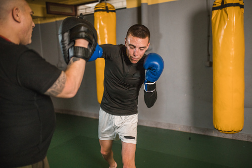 Healthy, fit and active male boxer training, exercising and sparring with his coach, trainer or instructor in the gym or health club. Man preparing for a boxing fight, match or competition