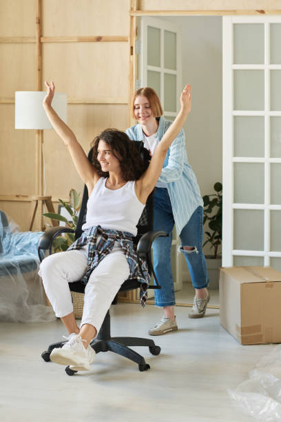 istock Young excited woman sitting on armchair while her girlfriend pushing it 1569780410