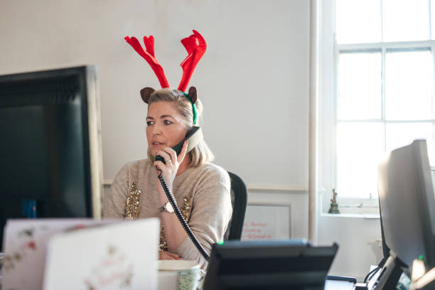 A front view medium close up of a female office worker who is making some last minute client calls before they break up for the Christmas break. She is in the festive spirit wearing her novelty antlers and Christmas jumper.
