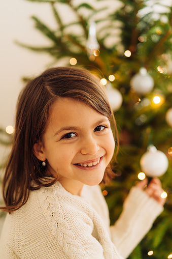 Sweet little girl peeking behind Christmas tree and smiling
