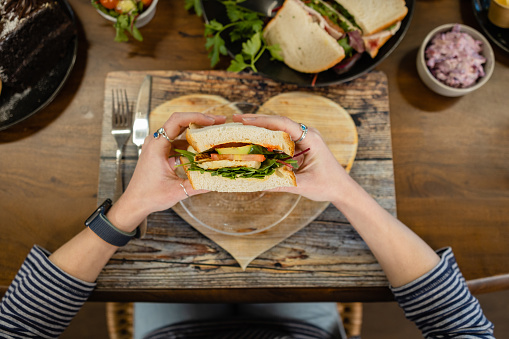 Personal perspective shot of a woman having lunch together at a cafe in Northumberland, North East England. She is eating a sandwich that has been plated on a wooden heart shaped board.