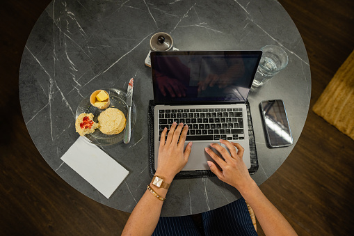 Directly above shot of an unrecognisable woman using a laptop at a cafe in Northumberland, North East England. She is enjoying a homemade scone while working.