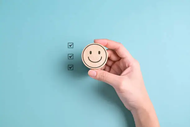 Photo of Hand holding happy smile face emotion on blue background, Customer service evaluation, Positive thinking and mental health assessment, Happy client giving feedback with happiness