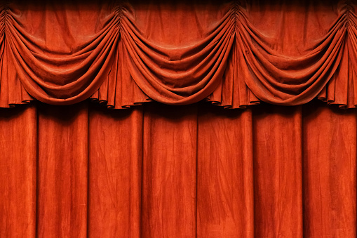 Closed red theatre curtains. Light from a spotlight falls on curved, bright, shiny, textile curtain backdrop. Image for presentation with copy space.