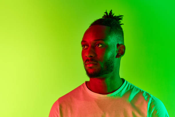 istock Portrait of young man with dreadlocks, guy with calm and face looking away over gradient yellow-green background in neon light. 1569844325