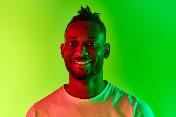 istock Close up of young african man with dreadlocks looking at camera with smile over gradient yellow-green background in neon. 1569844329
