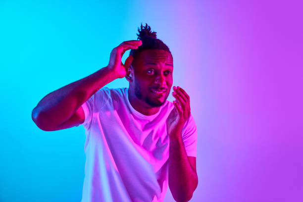 istock Scared frightened and covered with hands african man looking away over colorful studio background in neon. 1569844879