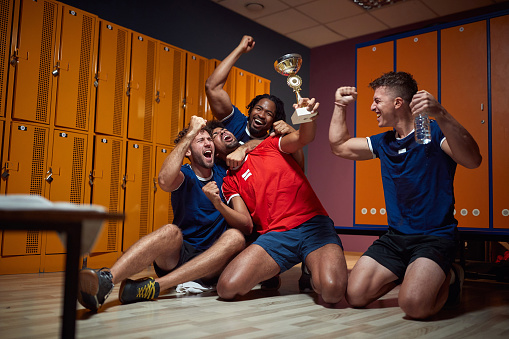 Young football players celebrating success together, hugging and cheering, holding golden trophy, feeling victorious in the dressing room. Sports, active lifestyle concept.