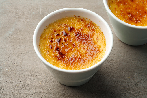 Creme brulee with caramel in two white bowls on gray background close up