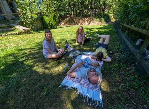 Group of male and female friends resting, napping, stretching and exercising on the ground of the green grass field on a sunny day in a natural mountain setting on a sunny day