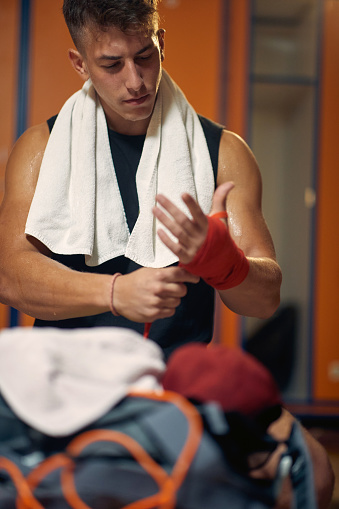 Muscular sporty young man tying red protective tape around hands for boxing. Martial arts, boxing, sports concept.
