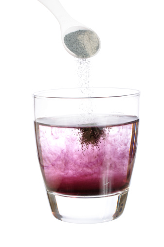 Spoonful of powdered grape soft drink mix falling into glass of water isolated on white
