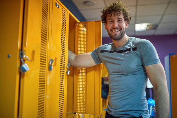 istock Cheerful young man standing in gym locker room, getting ready for workout session. 1569879001