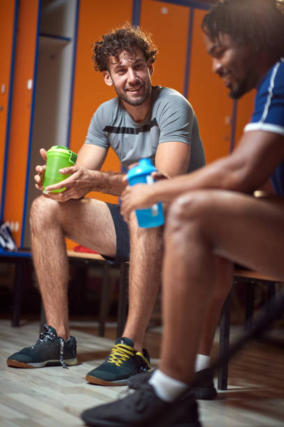 istock Young men in the locker room after workout, sitting on bench, resting. 1569887890