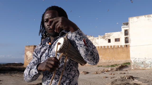 African percussion music, a Senegalese man playing a traditional small dunun drum with a stick.