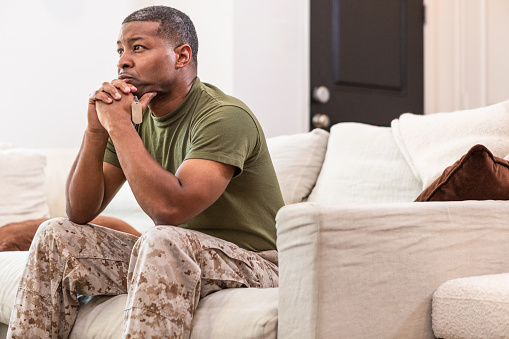 The worried male veteran sits alone in the living room and thinks about his daughter who is deployed currently.