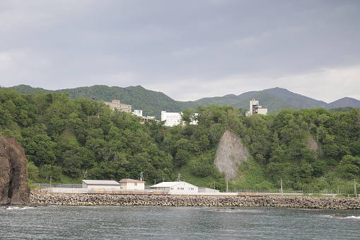 View from the bay at the Sea of Okhotsk to the waterfront at Utoro Fishing Port. A hotel district stands on the hill of Utorokagawa. The Shiretoko Mountains in the background are part of Shiretoko National Park. Spring afternoon in Hokkaido Prefecture.