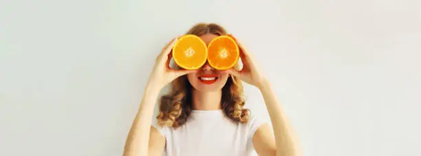 Summer, nutrition, diet and vegetarian concept. Happy healthy cheerful young woman covering her eyes with slices of orange fruits and looking for something on white background