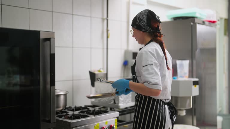 Young woman working and cooking food in commercial kitchen