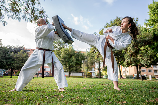 Teenage girl kicking a kick-shield while practicing karate/taekwondo at public park