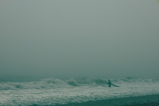 A silhouette of a surfer walking into turbulent stormy waves