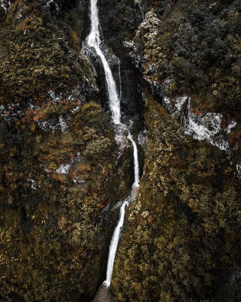 istock Aerial view of a lush hill with a thin, white waterfall cascading down 1569988220