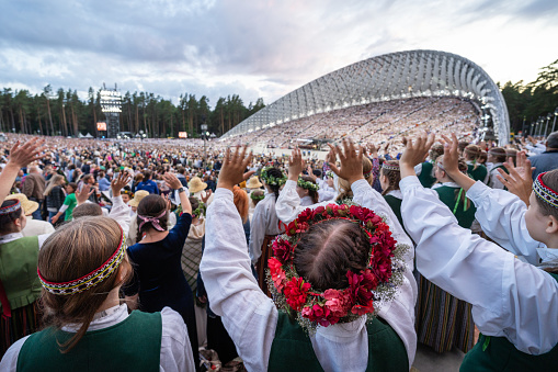 Riga, Latvia - July 9, 2023: In the foreground, the head of a young woman with a traditional wreath of flowers.