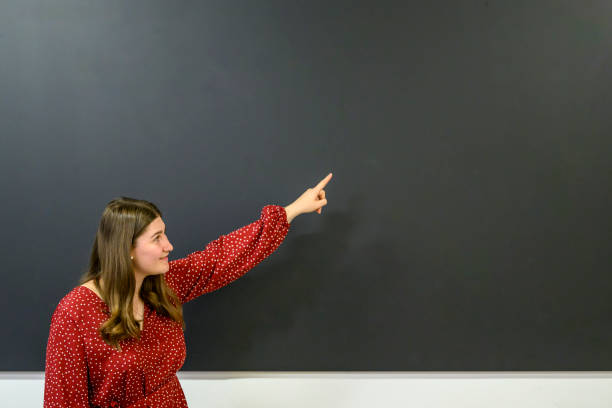 istock Smiling teacher showing something at the blackboard 1570005323