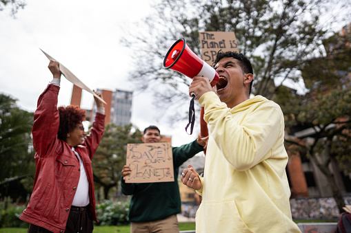 Young man shouting on megaphone on an environmental protest outdoors