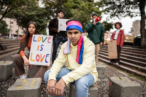 Portrait of a young protester man with a bisexuality flag on head during a protest outdoors