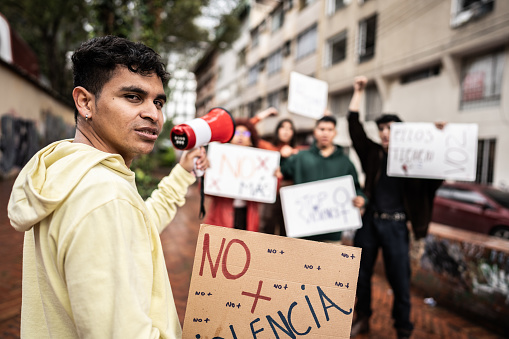 Portrait of a young protester man on a  demonstration with megaphone and banner outdoors