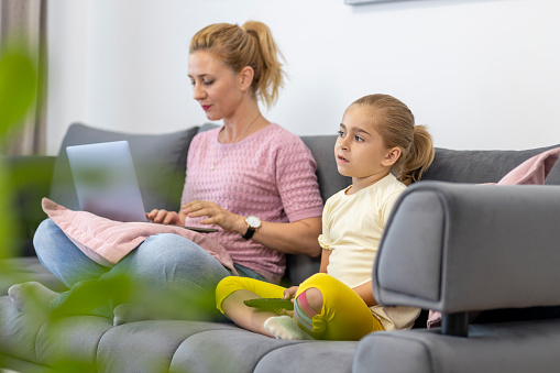 Girl watching TV  and her mother using laptop