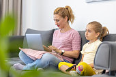 Mother smiling when working from home and daughter watching TV