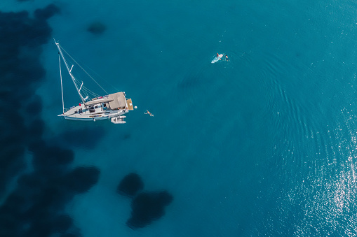 High-angle view of distant people swimming by modern sailboat on the sea