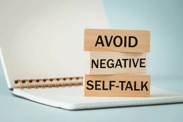 avoid negative self-talk written on wooden blocks standing on an open notebook, Avoid negative self-talk concept, Light blue background, copy space