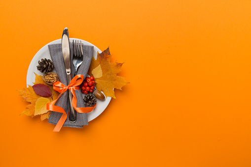Plate with cutlery, napkin and autumn decor on color background, top view. Thanksgiving table setting