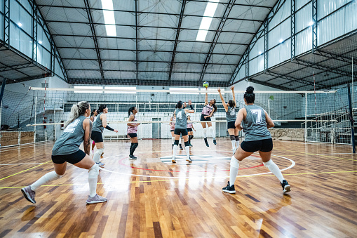 Female volleyball player spiking the ball while other team defending at sports court
