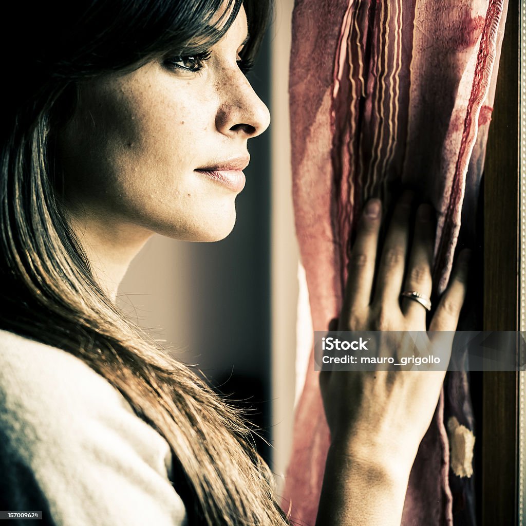 Pensoso donna guardando attraverso una finestra - Foto stock royalty-free di Adulto