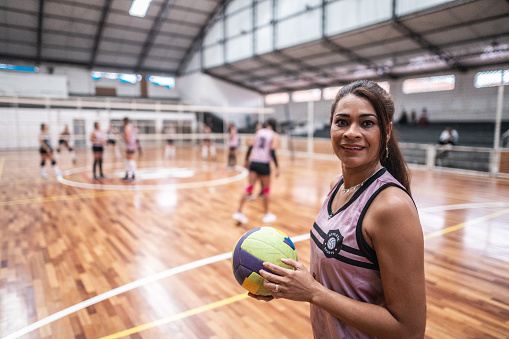 Portrait of a mature female volleyball player holding the ball on the sports court