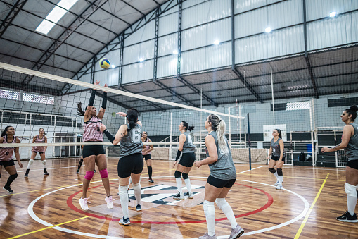 Low angle view of a volleyball players' hands blocking a ball over the net on training. Close up of sportswomen hands with a volleyball blocking it over the volleyball net during the training.