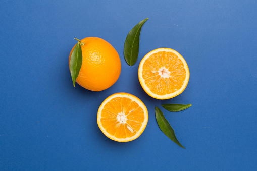 Flat lay with fresh oranges and leaves on color background.