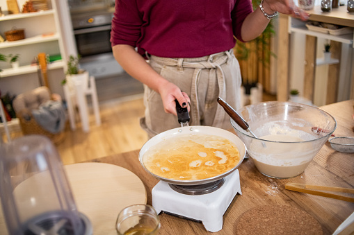 A young beautiful woman is preparing pancakes, the kitchen counter is covered with colorful ingredients and the smell of freshly baked pancakes fills the room.