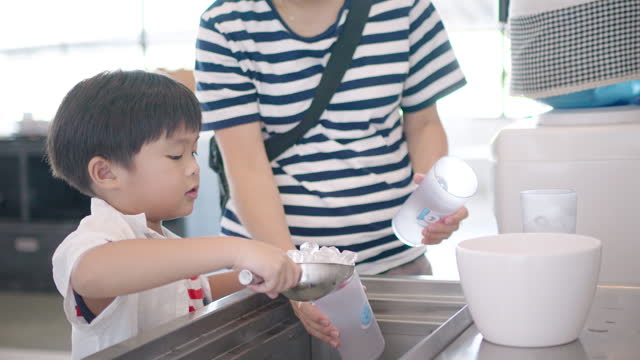 A little boy pouring pieces of ice into it using a stainless steel scoop.