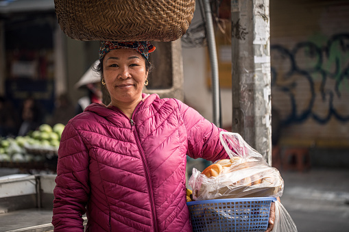 Hanoi, Vietnam - November, 28. 2018: Street vendor, Vietnamese woman with a big baskets full of fruits on her head and in hands