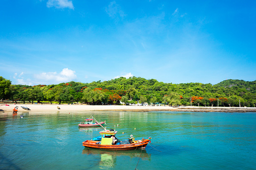 Two thai fishermen in small boat at coast of Ko Sichang. People are anchoring near historical pier and beach close to Phra Chutha Thut Rat Than Museum from around 1900 at east coast. In background is rainforest on hill