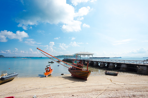 Side panorama of Historical  wooden  pier สะพานอัษฎางค์ with small fishermen boats at beach on Ko Sichang island in Chonburi province. Pier is historical attraction near Phra Chutha Thut Rat Than Museum from around 1900 at east coast